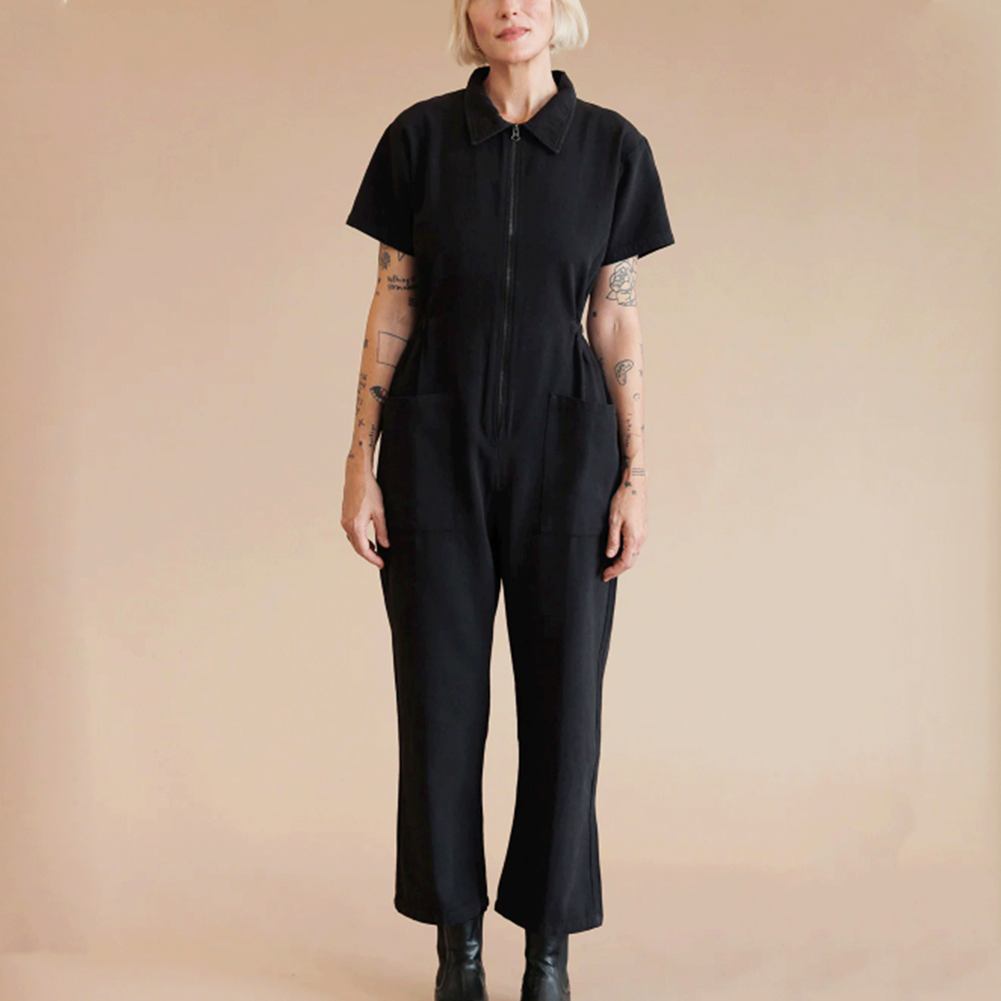 A model wearing a black short sleeve utility jumpsuit with a front zipper detail.