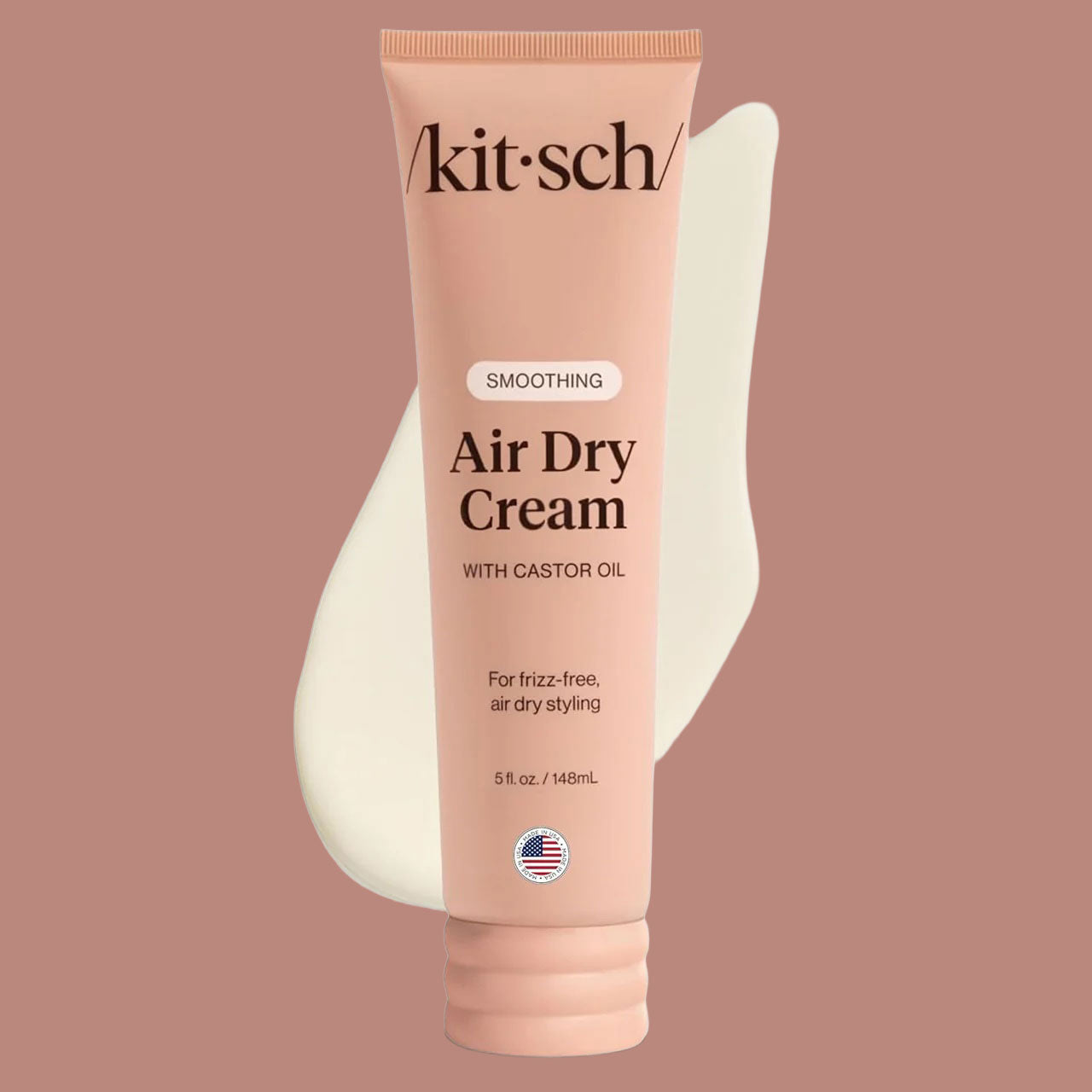 Peach-pink tube of Kitsch ‘Smoothing Air Dry Cream with Castor Oil’ standing in front of a white cream swatch on a mauve background.