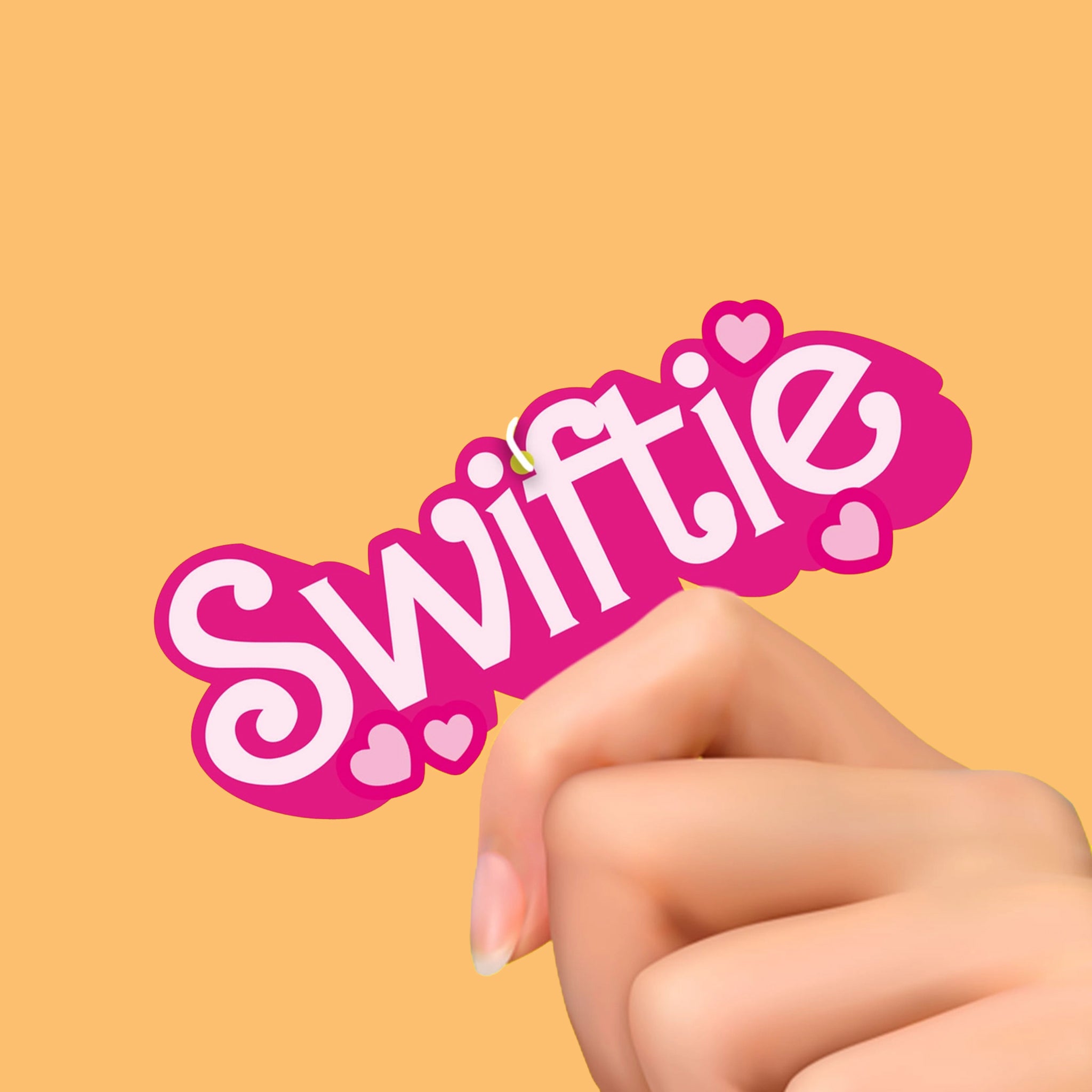 A pink and white air freshener out of its plastic packaging that reads, "Swiftie".
