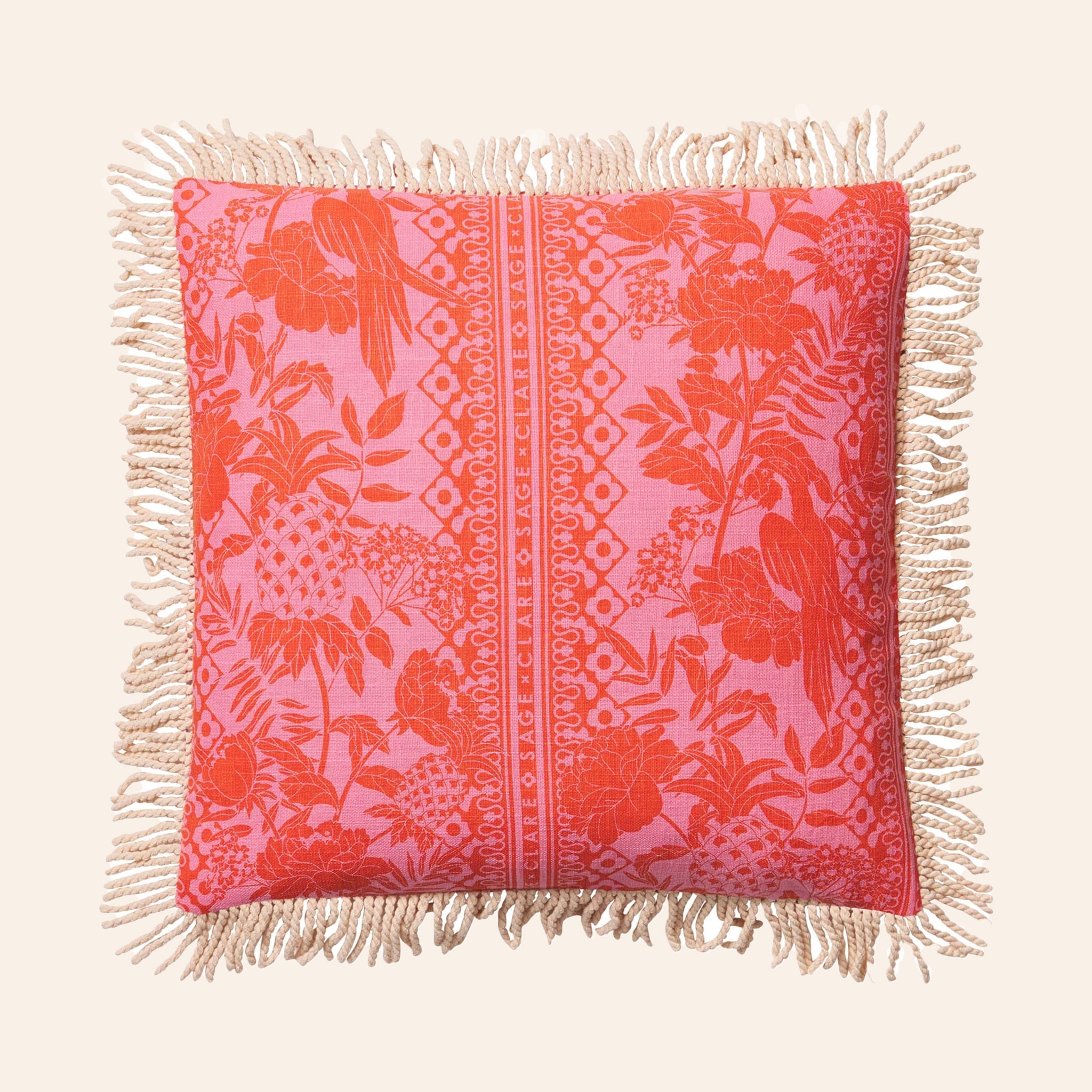A pink and orange tropical print pillow with a. tassel edge. 