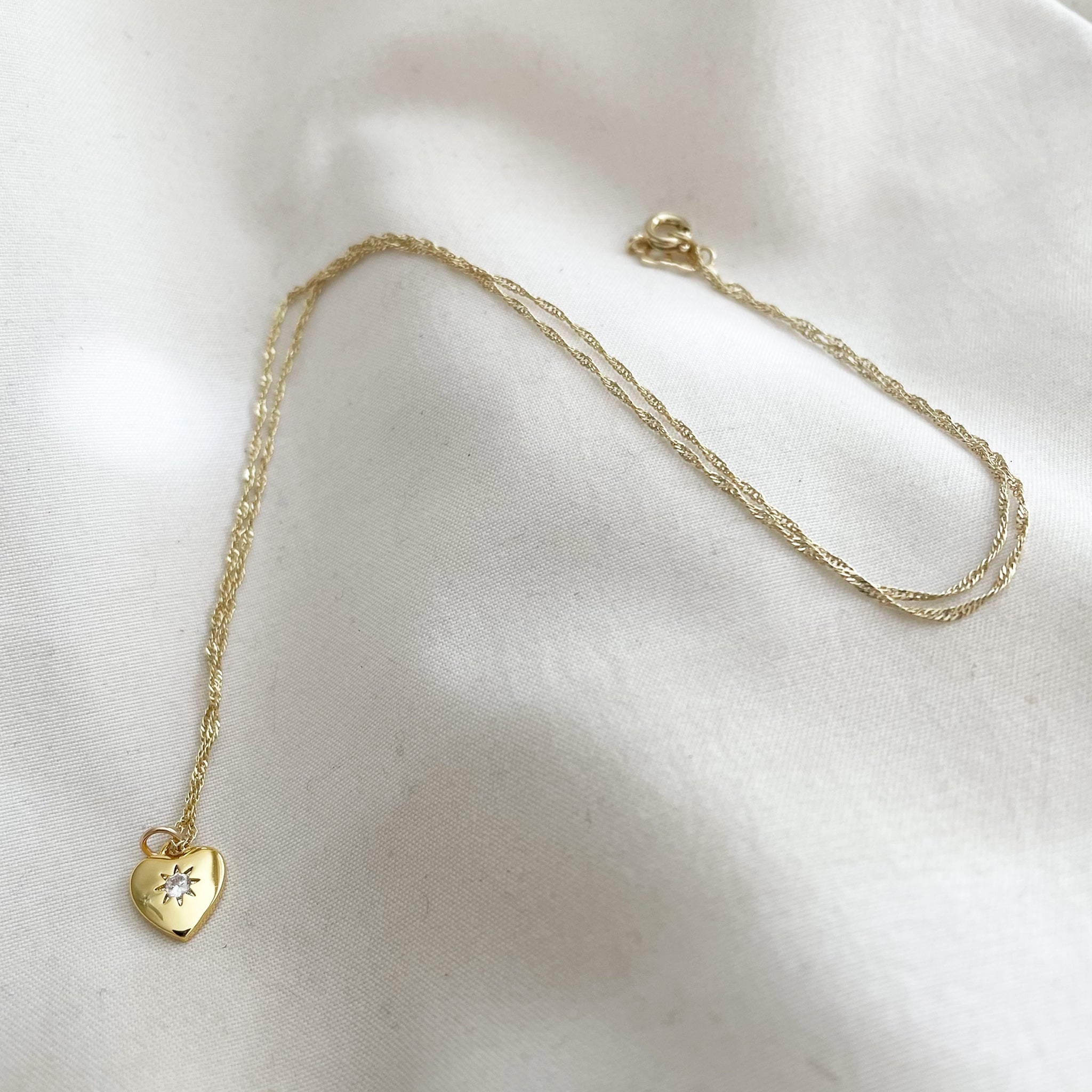 Gold necklace with a heart-shaped pendant on a white fabric background