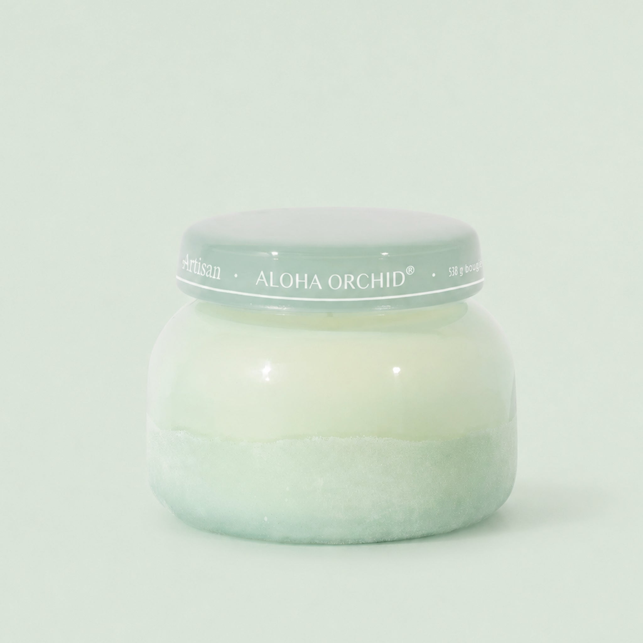 Green candle in a glass jar with white flowers on a reflective surface