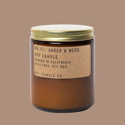 On an orange background is an amber glass jar candle with a kraft brown label and a gold lid. 