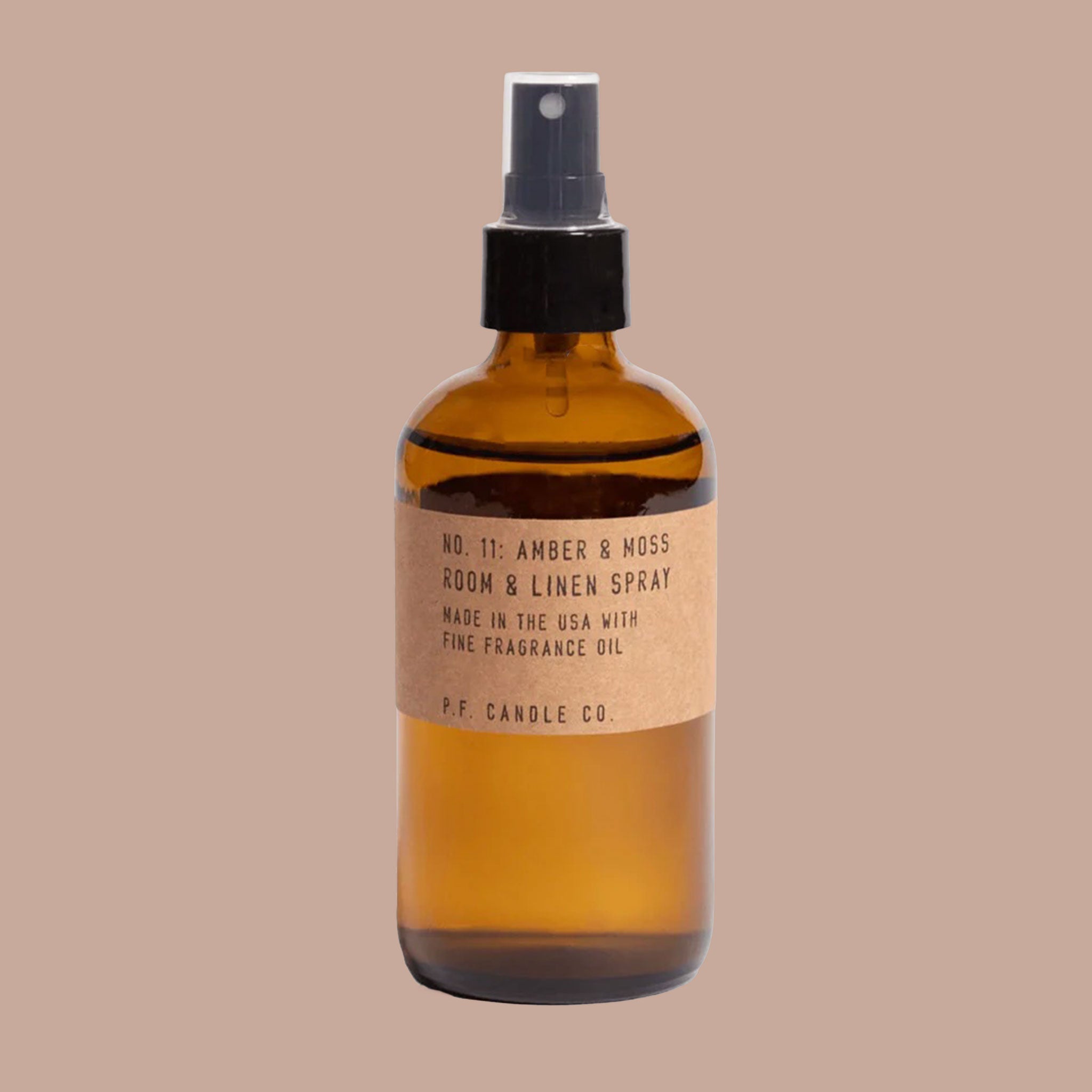Small translucent brown spray bottle with black push spray nozzle. Brown paper label with text, "Number 11 Amber and Moss, Room and Linen Spray, made in the USA with fine fragrance oil. PF CANDLE CO."