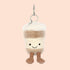 On a pink background is a stuffed toy in the shape of a to-go coffee shape. 