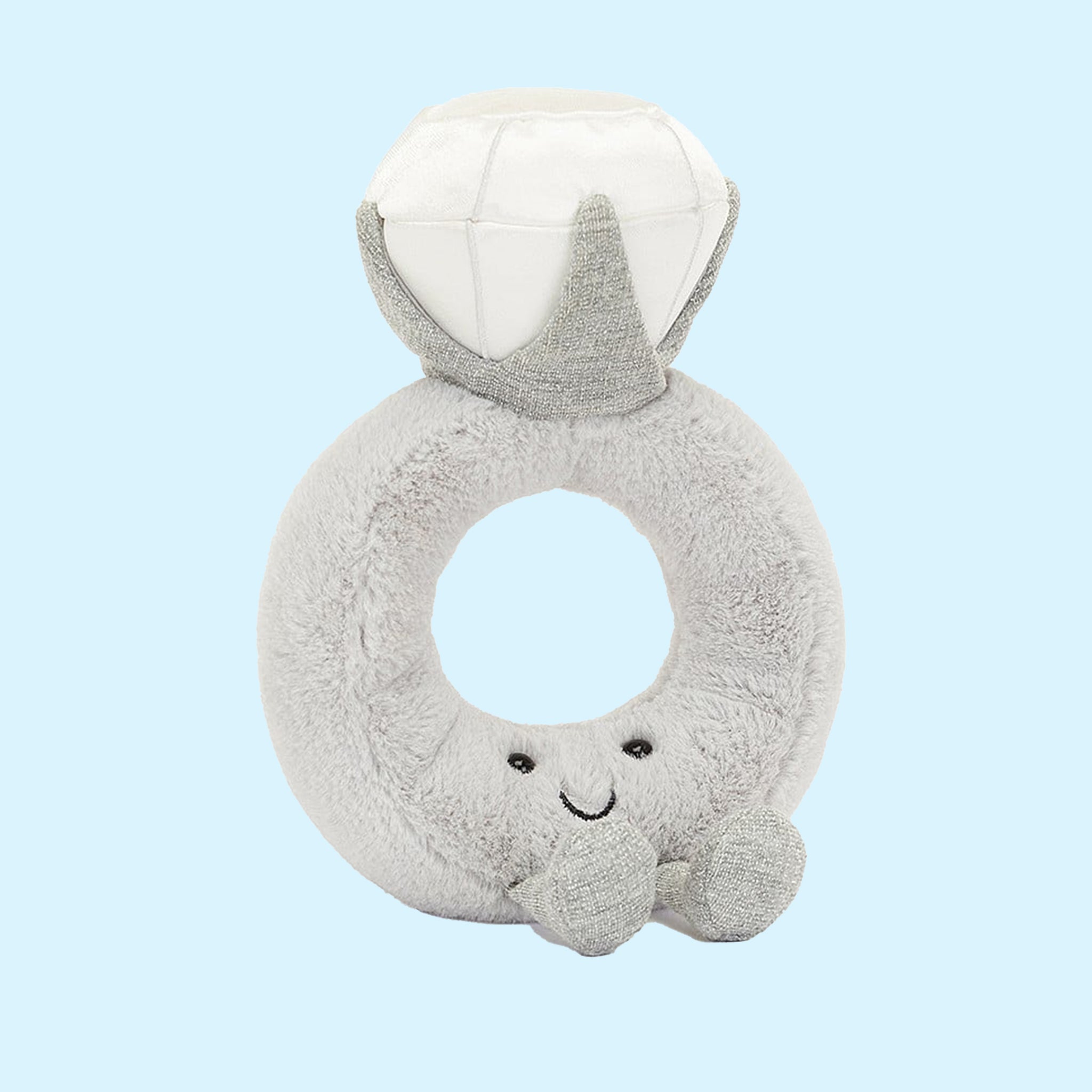 A grey stuffed toy in the shape of a diamond ring with a grey band and a white diamond shape along with a smiling face and feet on the front. 