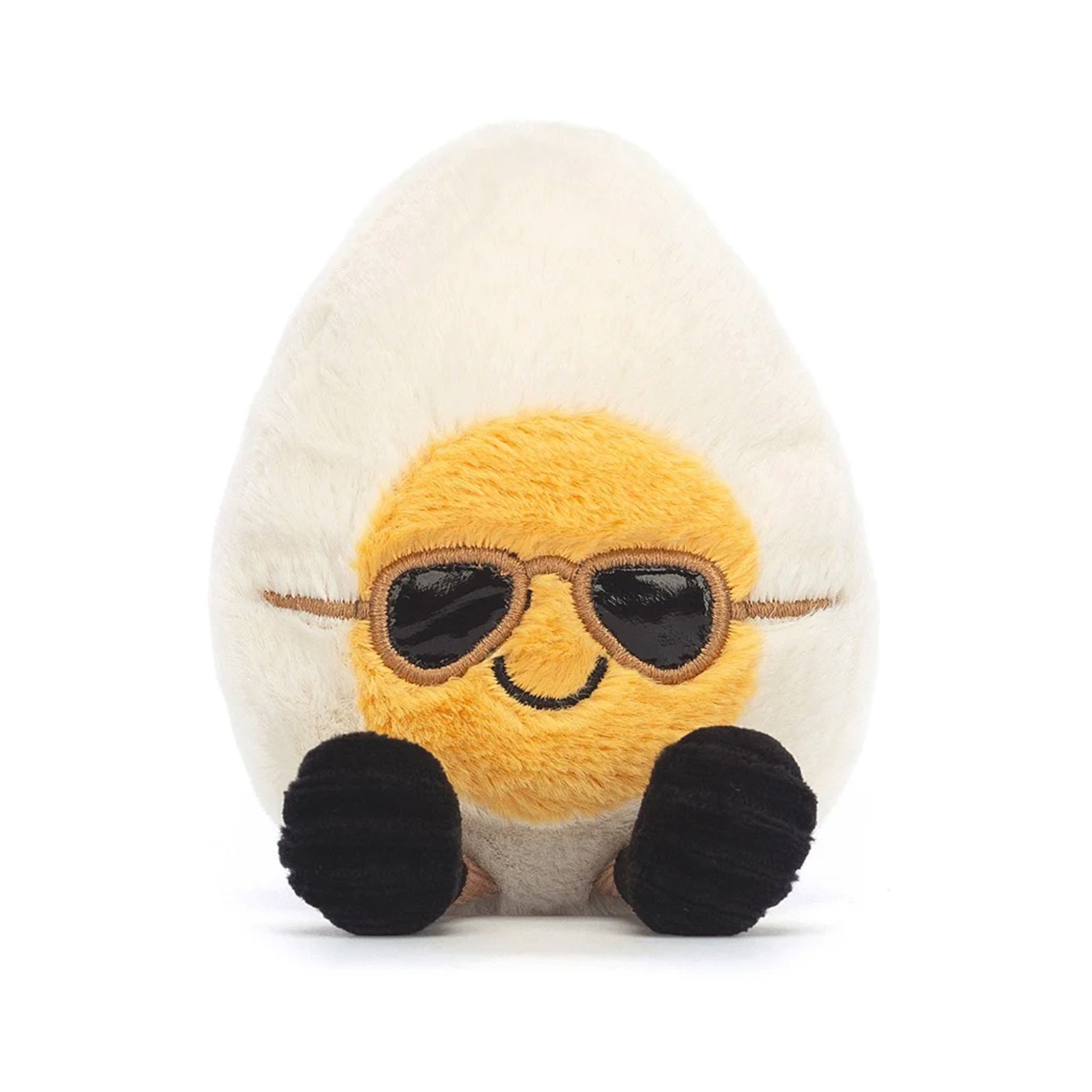 On a white background is a stuffed toy in the shape of a hard boiled egg with sunglasses on and small legs and feet. 