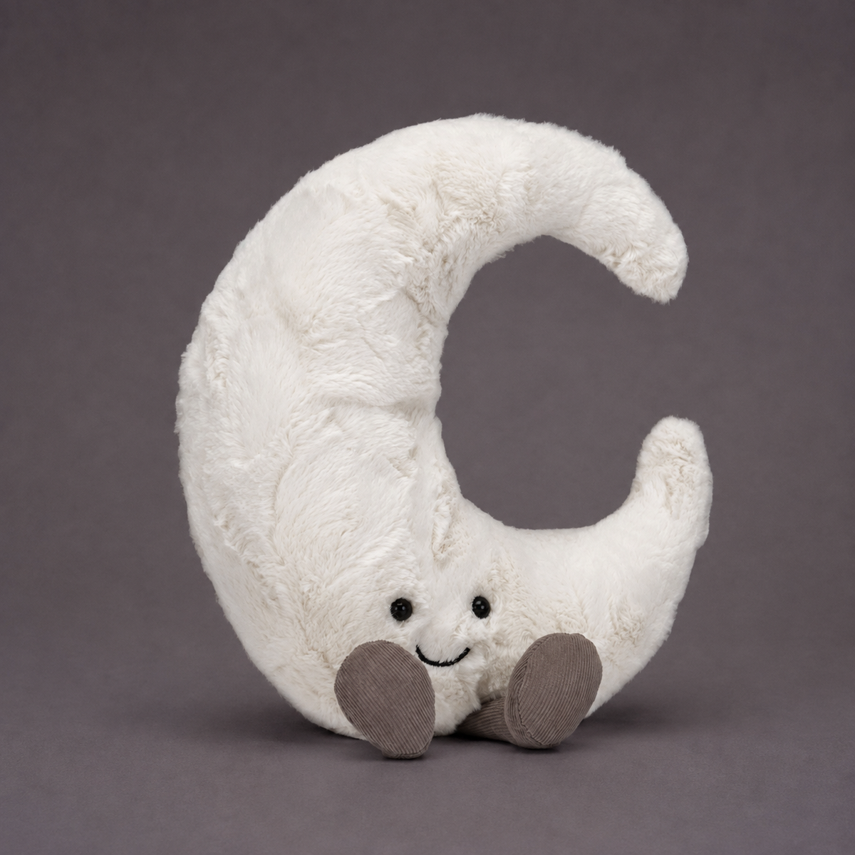 An ivory crescent moon shaped stuffed toy with a smiling face and brown feet. 
