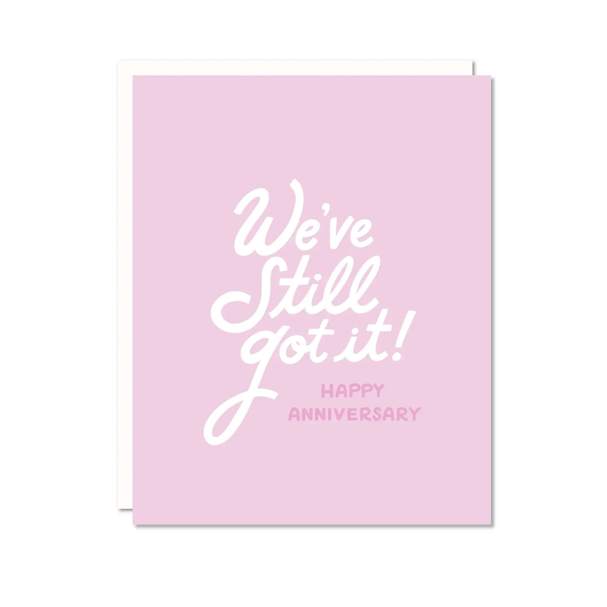 On a white background is a light pink card with white text that reads, "We've Still Got It! Happy Anniversary". 