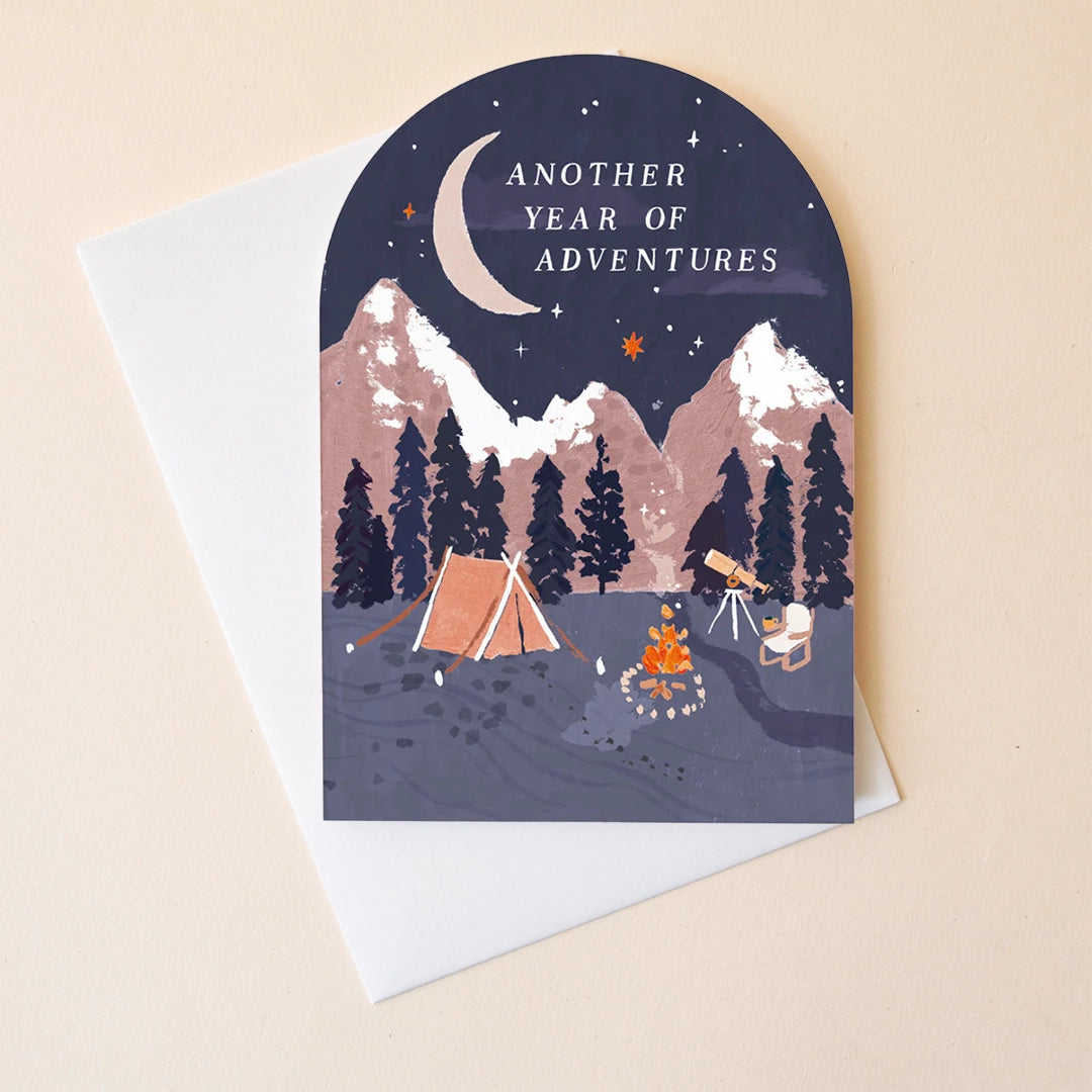 On a neutral background is an arched shape card with an illustration of a campsite in a mountainous region and white text at the top that reads, &quot;Another Year of Adventures&quot;. 