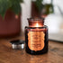 A black glass jar with a bronze label in the center. 