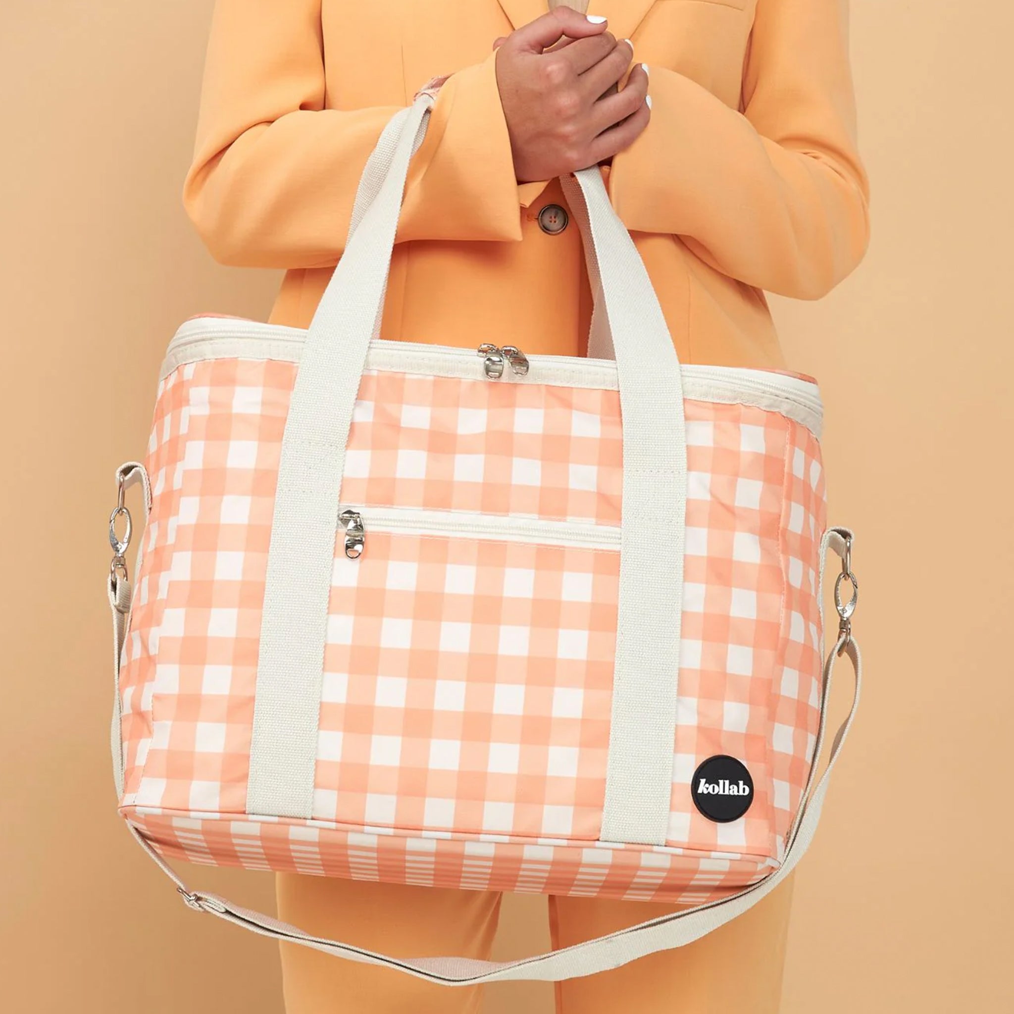 An ivory and apricot checkered print picnic bag with white straps and zippers. 