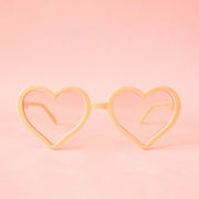 On a neutral background is a pair of apricot heart shaped glasses.