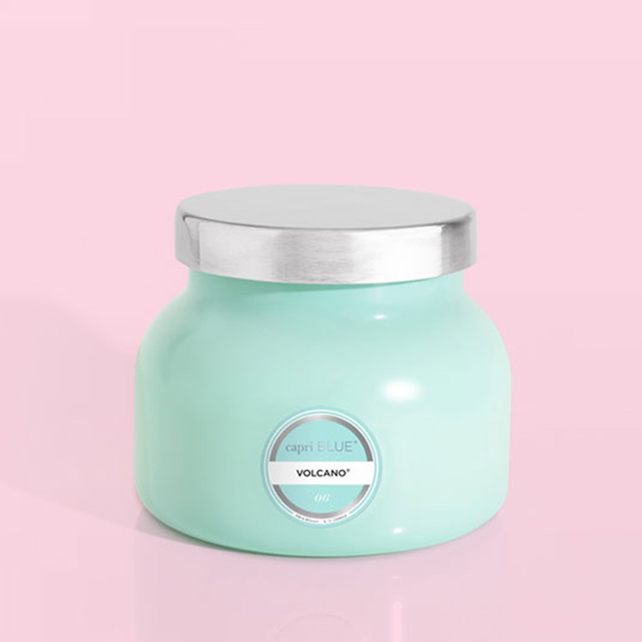 On a pink background is the smaller version of the aqua blue glass jar candle with a silver lid on top.