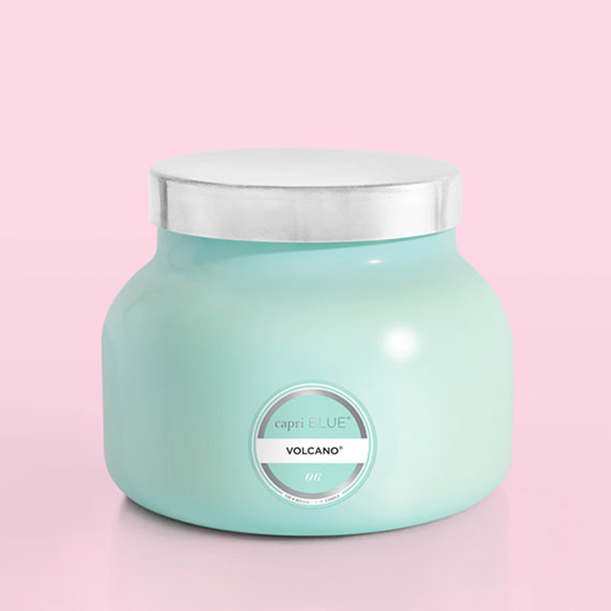 On a pink background is an aqua blue glass jar candle with a silver lid on top.
