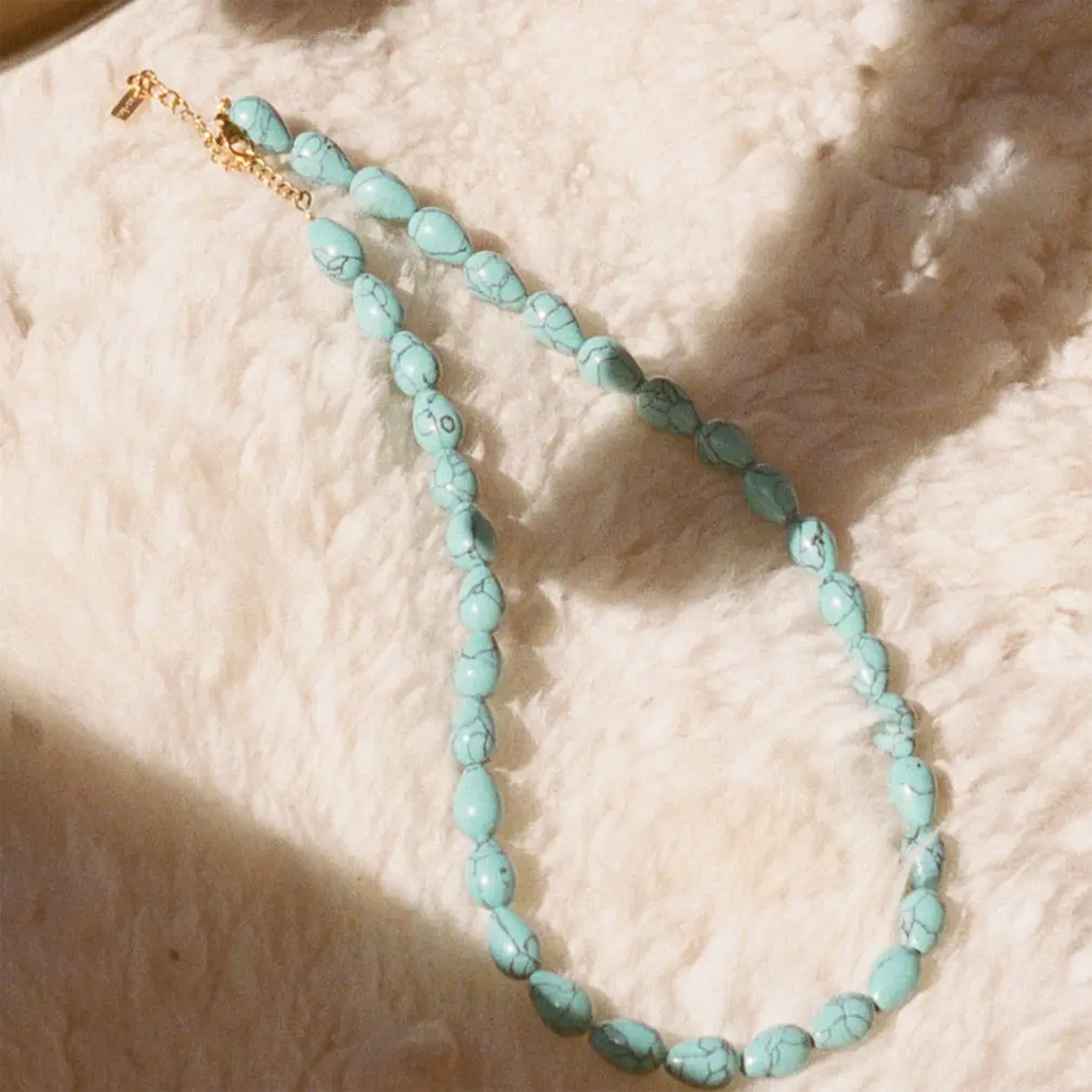Turquoise beaded necklace on a textured beige surface