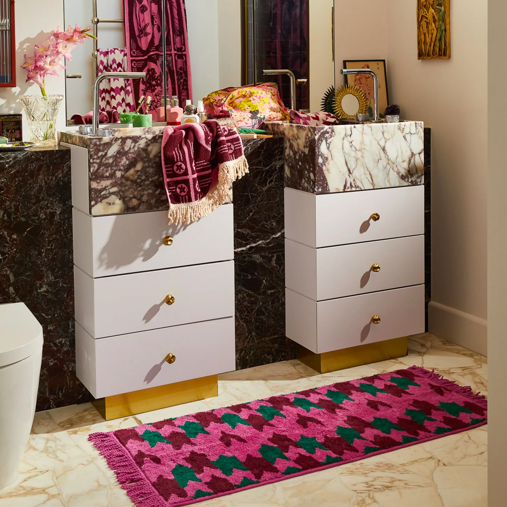 Bright pink, dark pink and dark teal bath mat with pink fringe shown in a bathroom.