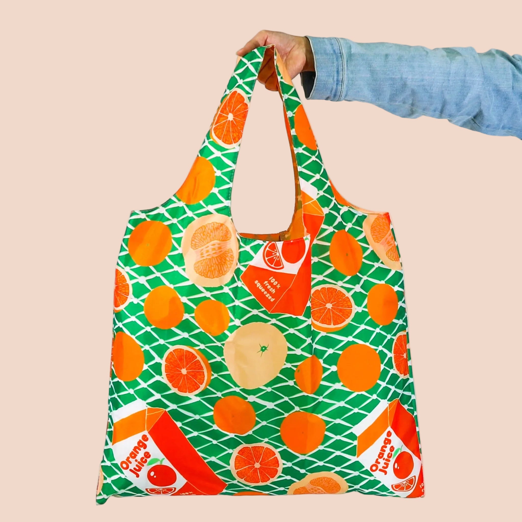 A green and orange foldable tote bag with orange slices and orange juice carton graphics. 