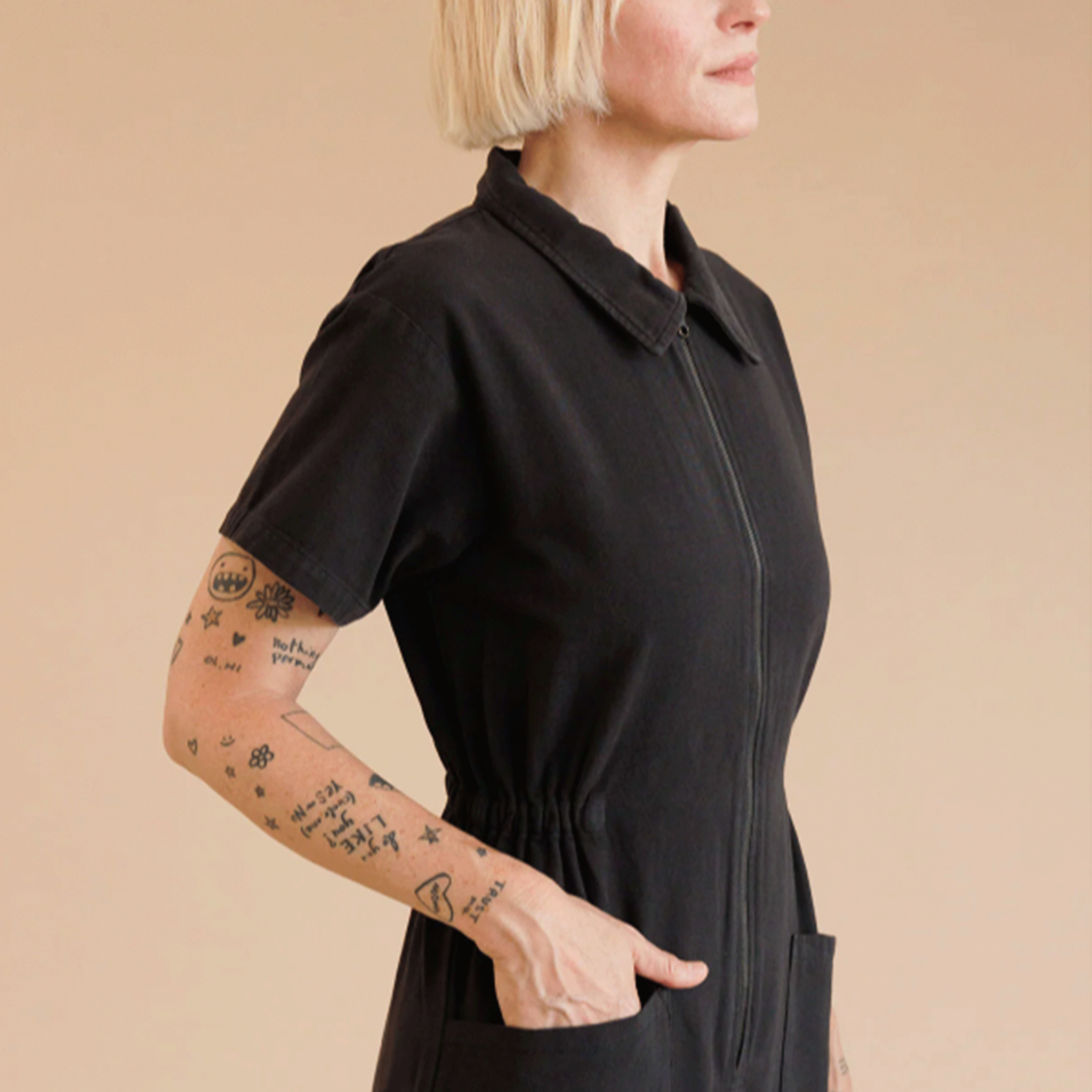 A model wearing a black short sleeve utility jumpsuit with a front zipper detail.