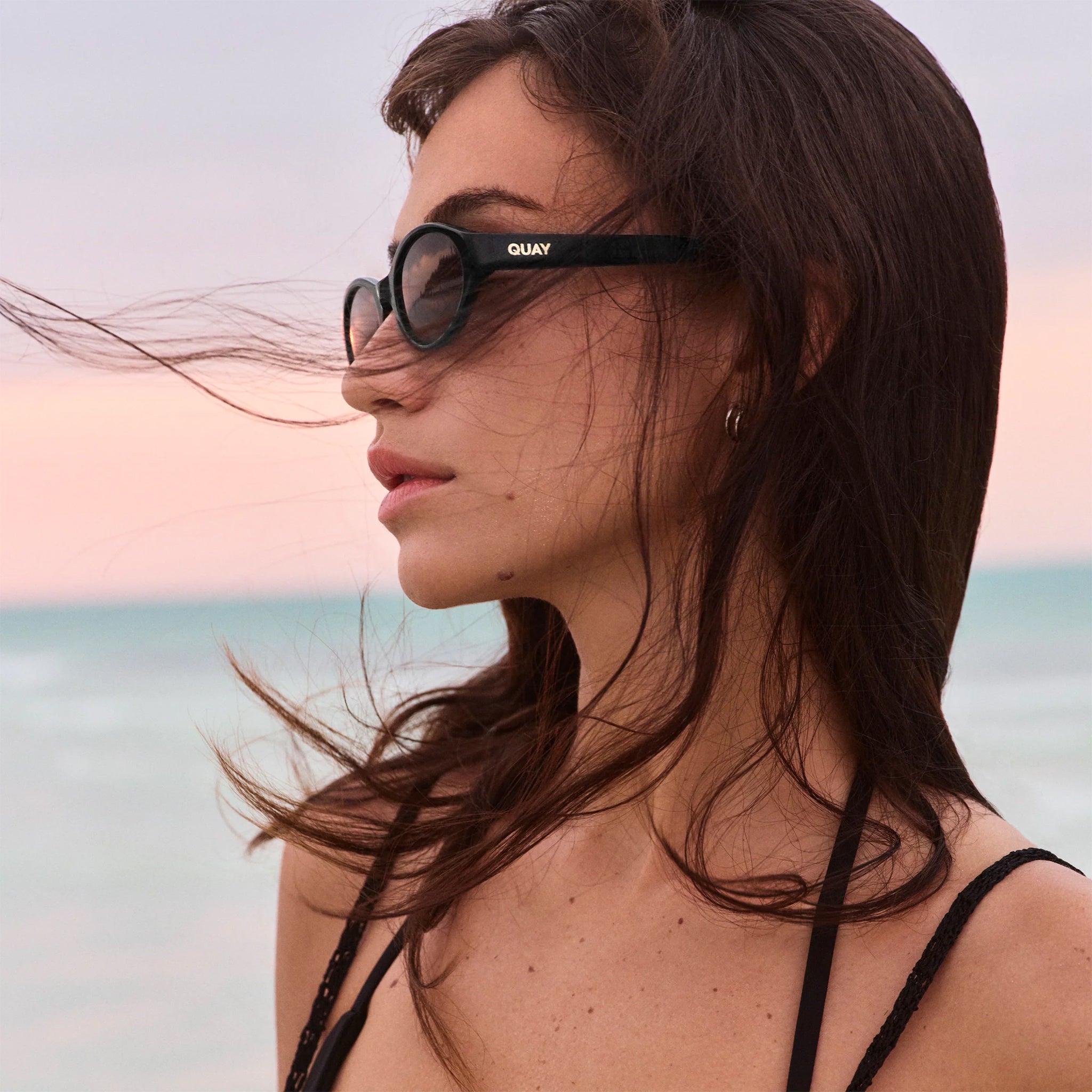 A pair of black oval shaped sunglasses with a dark grey lens. 