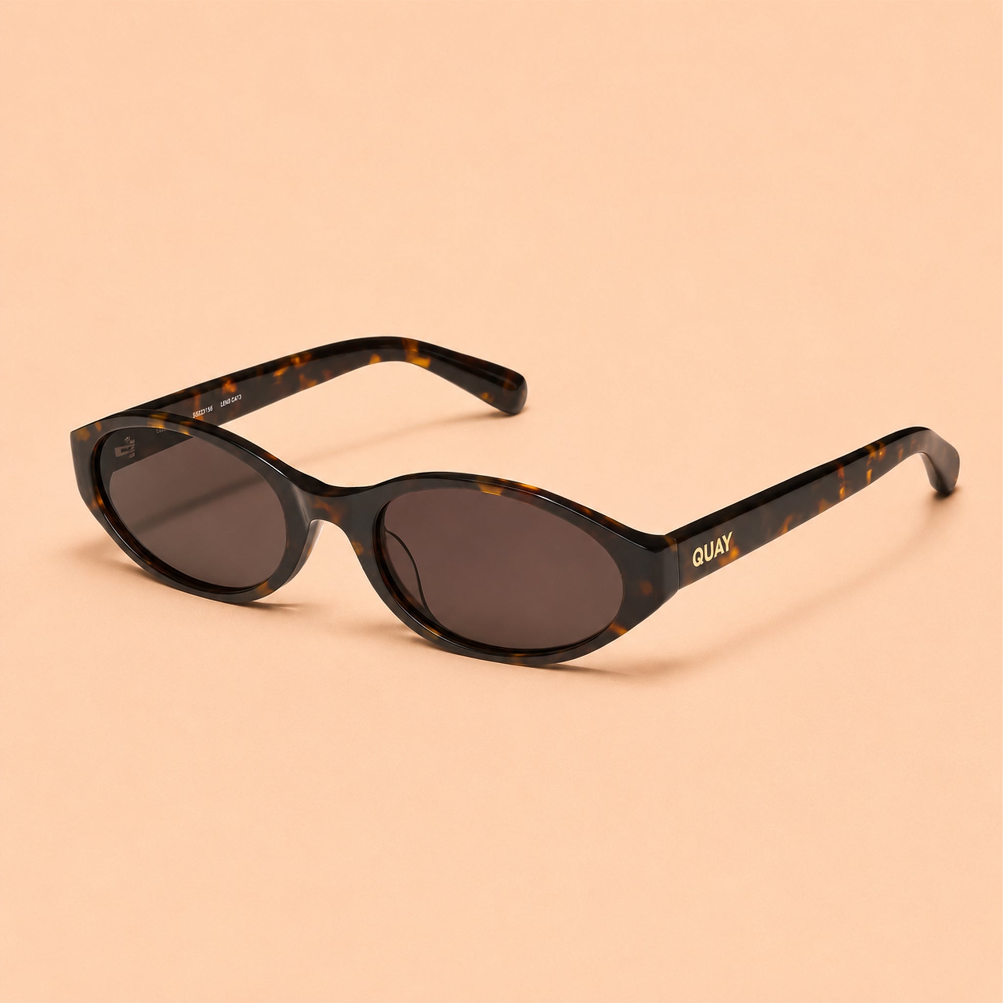 Brown sunglasses with a visible brand Quay logo on a light tan background