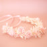 A flower crown crafted from white and pink colored dried florals and a light pink ribbon for tying in the back. 