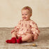 A light peach colored long sleeve romper with a red floral print. 