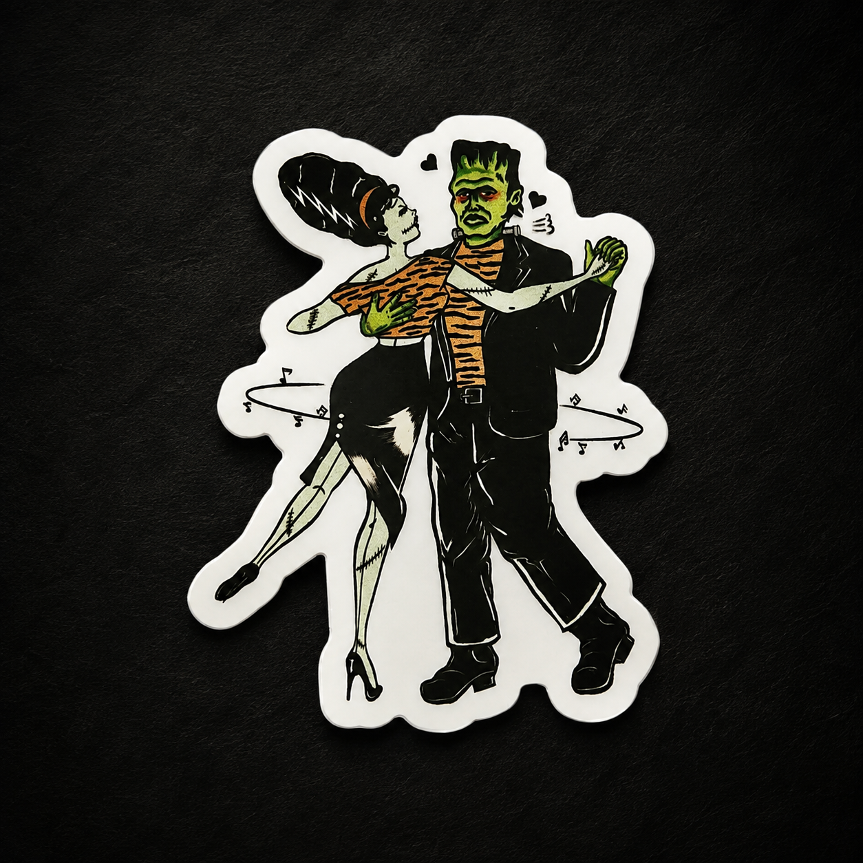 a sticker of frankenstein and his girlfriend dancing on a black background.
