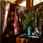 Brown towel with a leaf pattern draped over a tiled bathroom partition beside a sink with plants and decor.