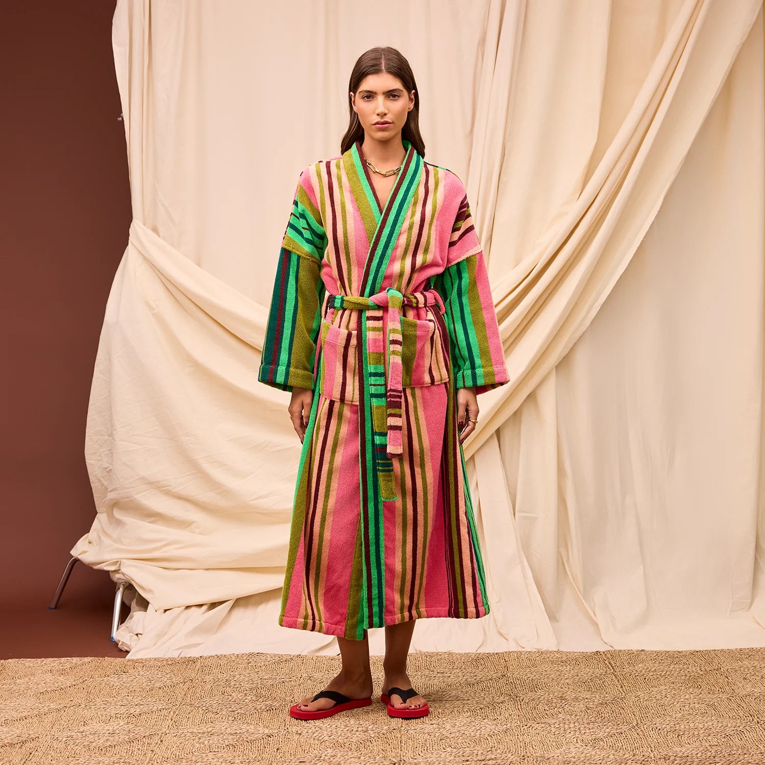 A person standing in front of a canvas tapestry wearing a striped robe featuring pink and green stripes.