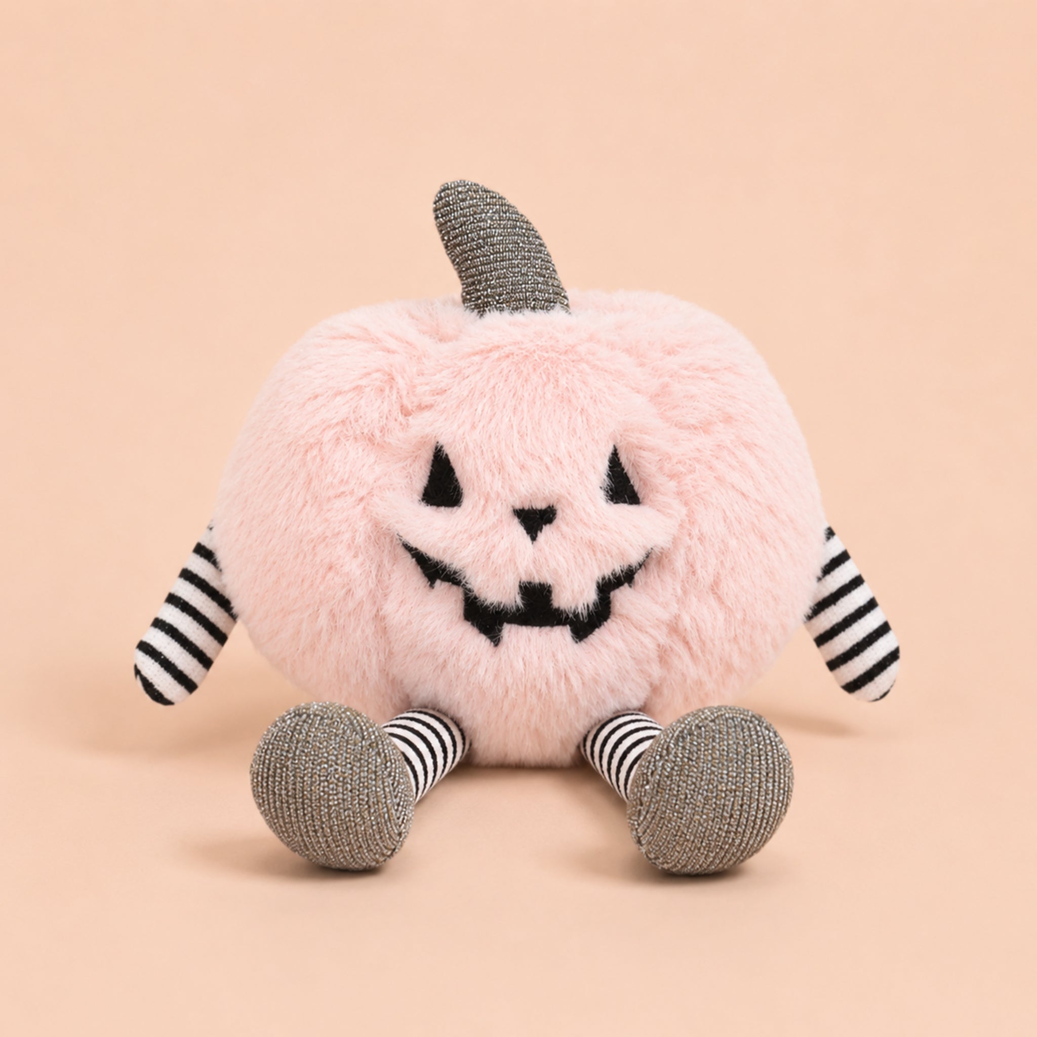 A light pink pumpkin stuffed toy with striped arms and legs. 