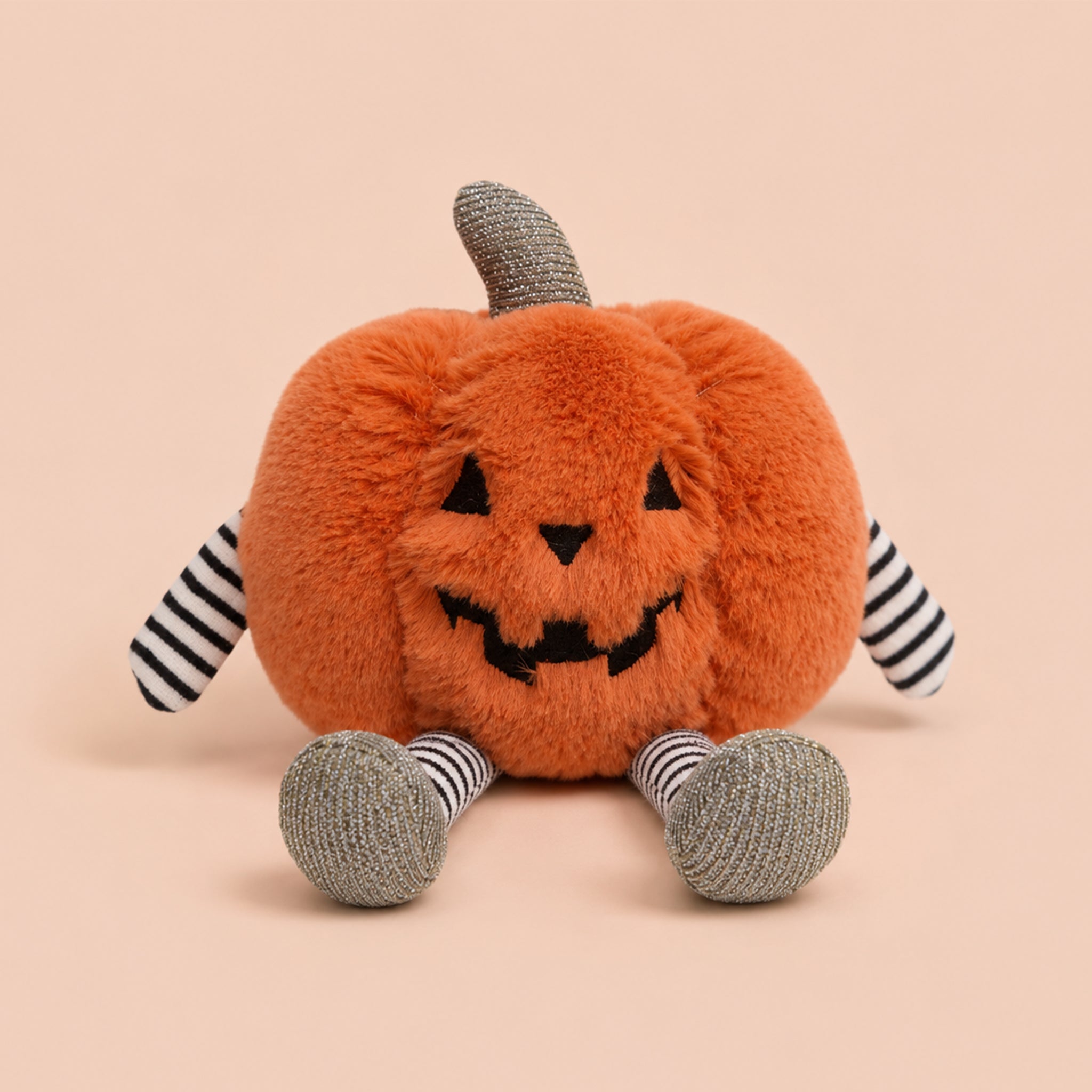 A mini orange pumpkin shaped character stuffed toy with black and white stripe legs and arms. 