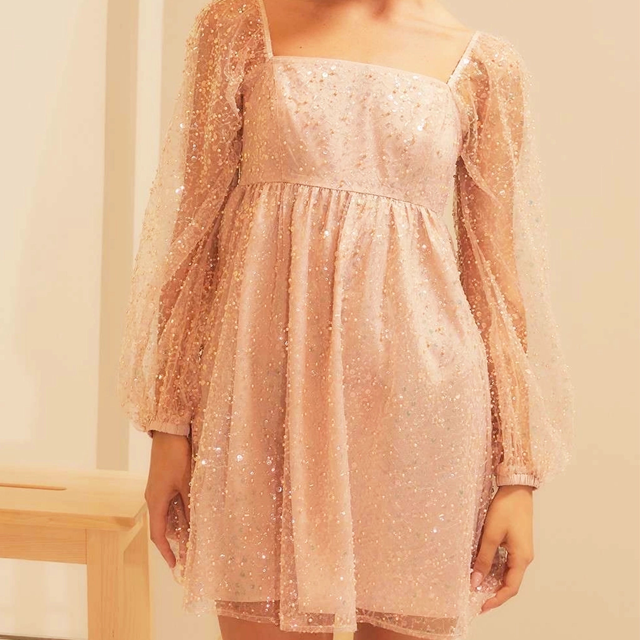 On a neutral background is a peachy pink babydoll dress with sleeves and a square neckline.