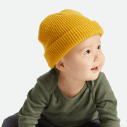 On a white background is a baby wearing a yellow knit beanie. 