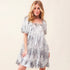 On an ivory background is a model wearing a silver sequin dress with a square neck and puff sleeves. 