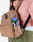 A nylon backpack in a tannish brown color with black straps and two front zipper compartments.