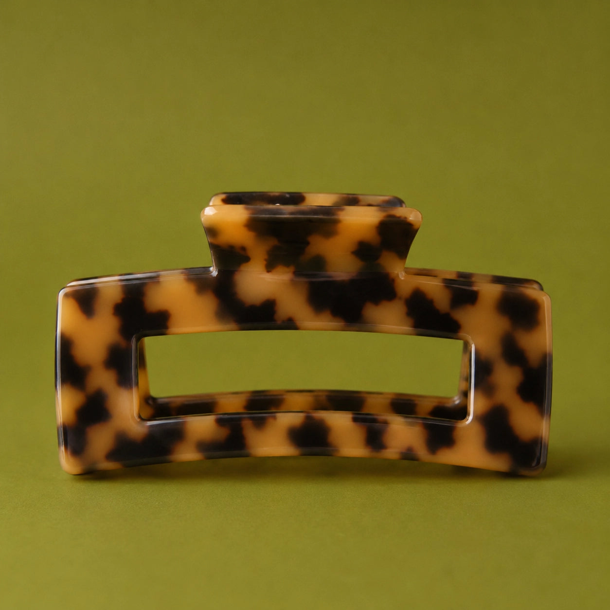 A tortoiseshell hair claw clip with a glossy amber-brown and black pattern, photographed against a solid olive green background.