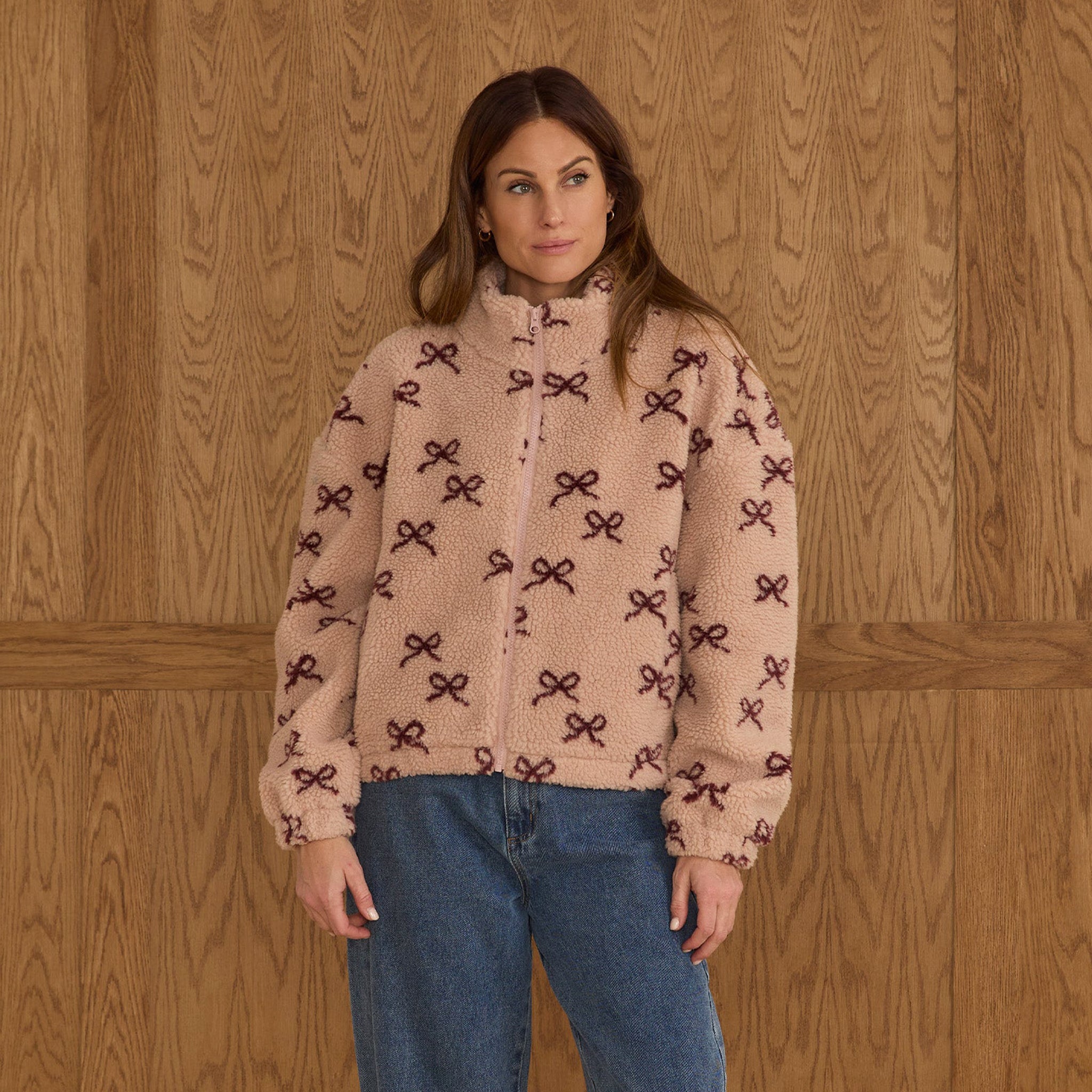 A beige, pink shearling jacket with burgundy bow details. 