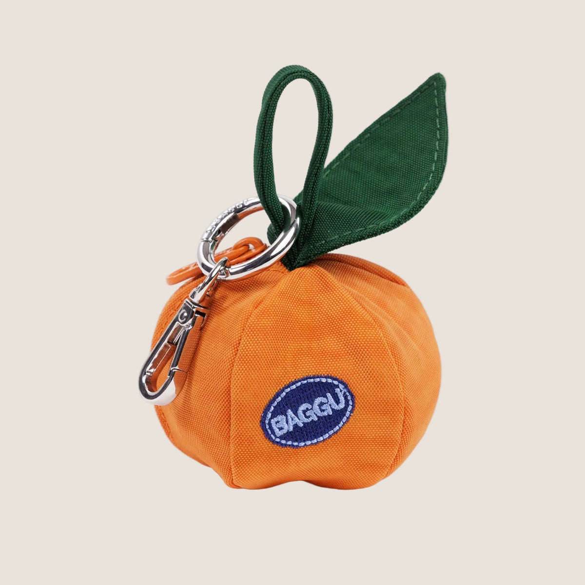 A round mandarin orange shaped bag charm that reads, "Baggu" embroidered on a blue patch. 