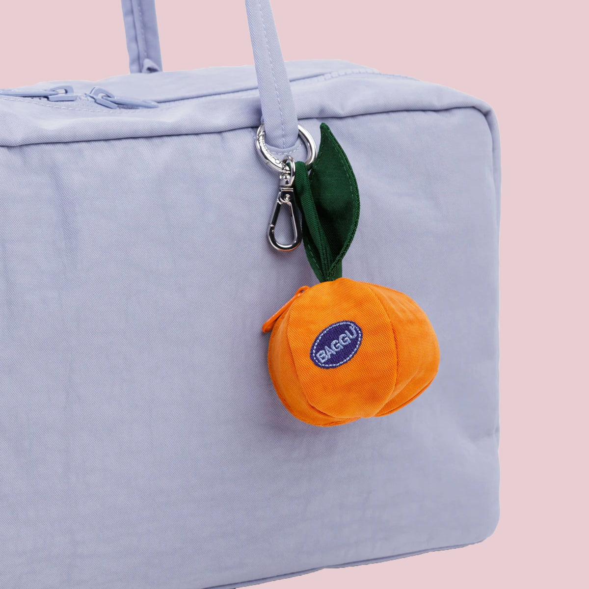 A round mandarin orange shaped bag charm that reads, "Baggu" embroidered on a blue patch with a silver keychain. 