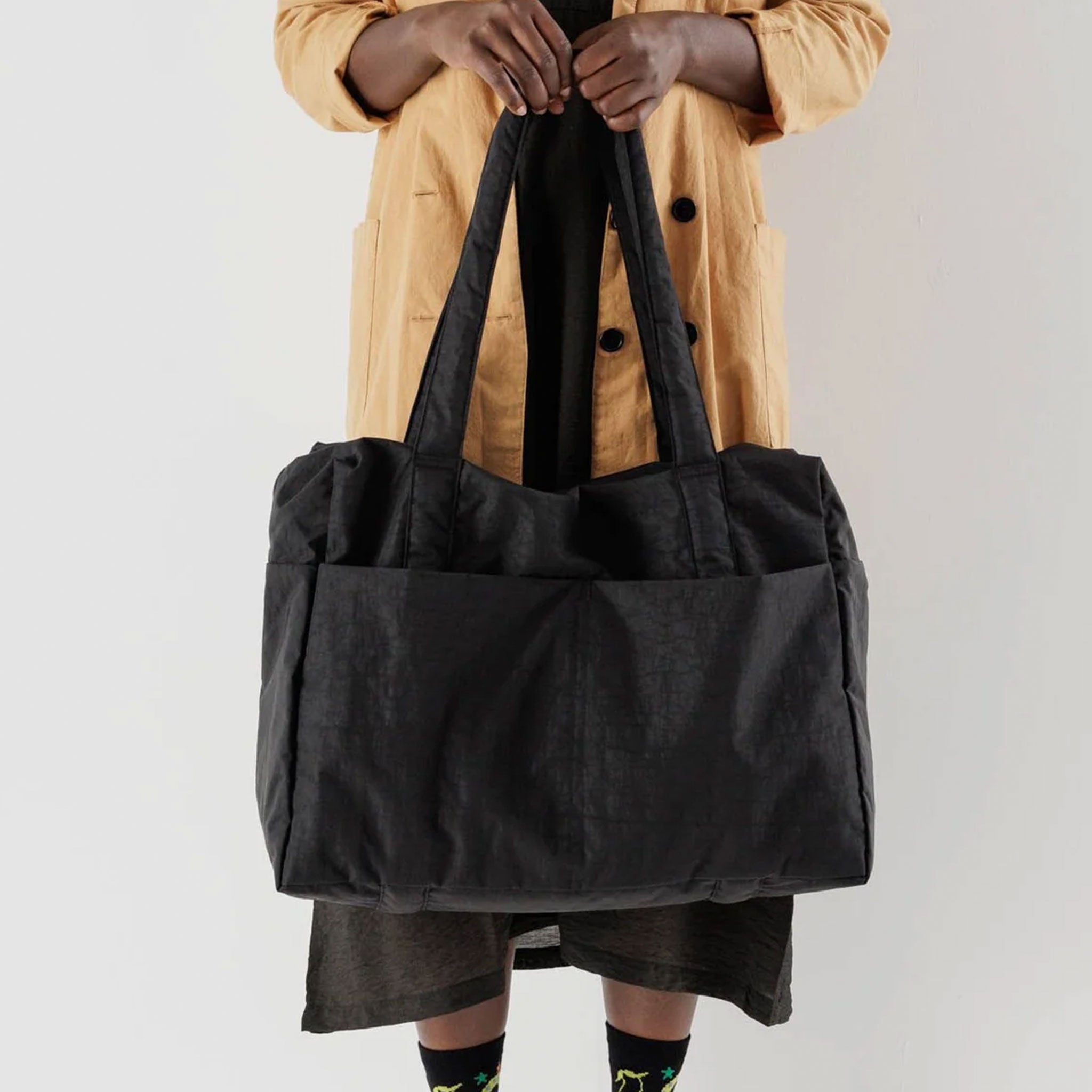 A black nylon tote bag with two straps and slits for attaching to a travel suitcase. 
