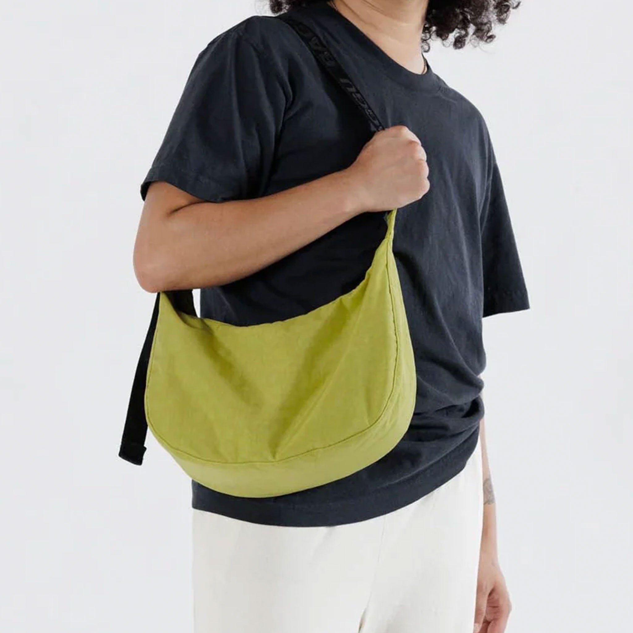 A model wearing a A crescent shaped bag in a lime green color with a black strap.