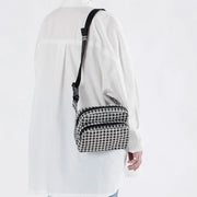a black and white gingham print fanny pack with black strap hangs off of a person's shoulder