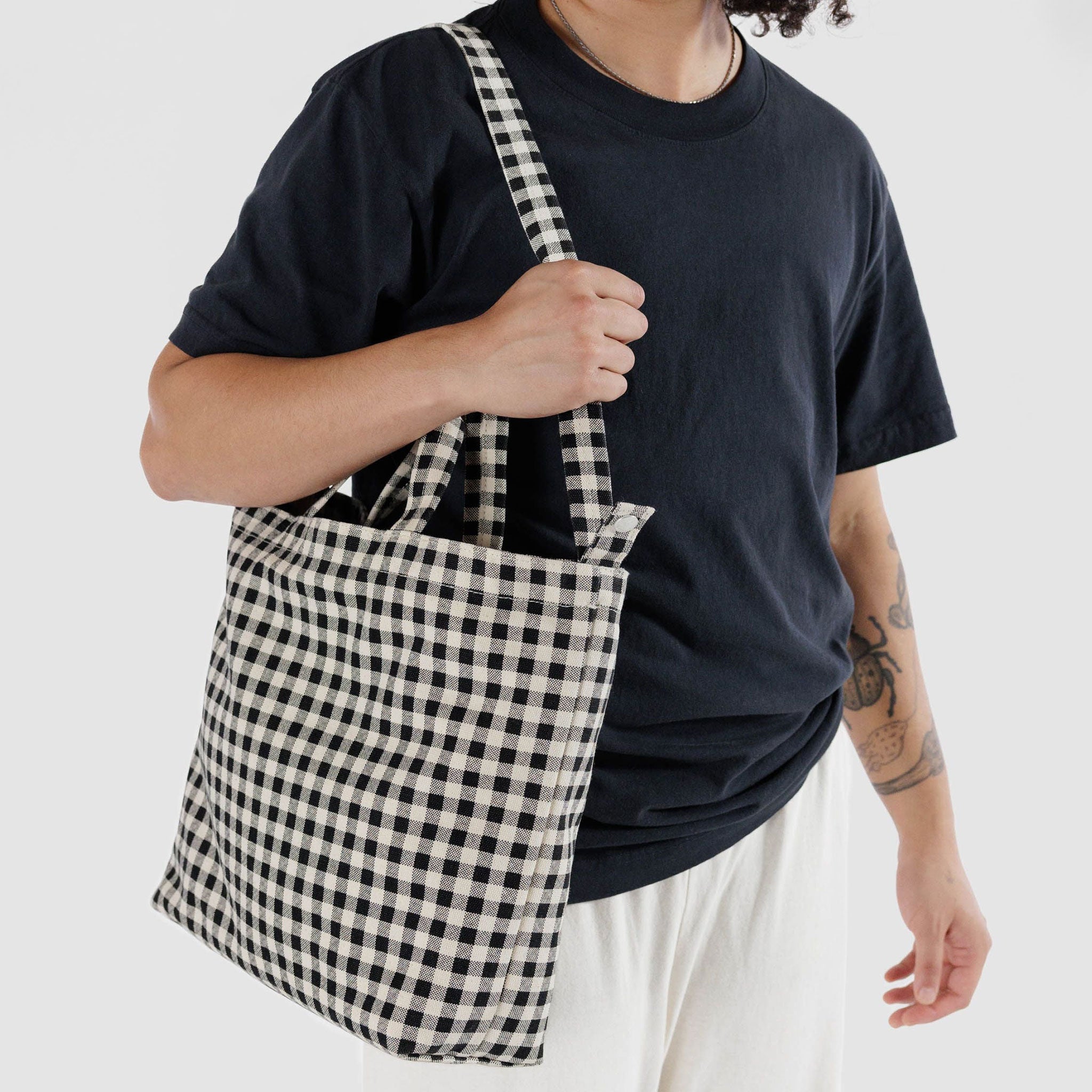 On a white background is a black and white gingham printed canvas bag with a hand strap and a longer adjustable shoulder strap.