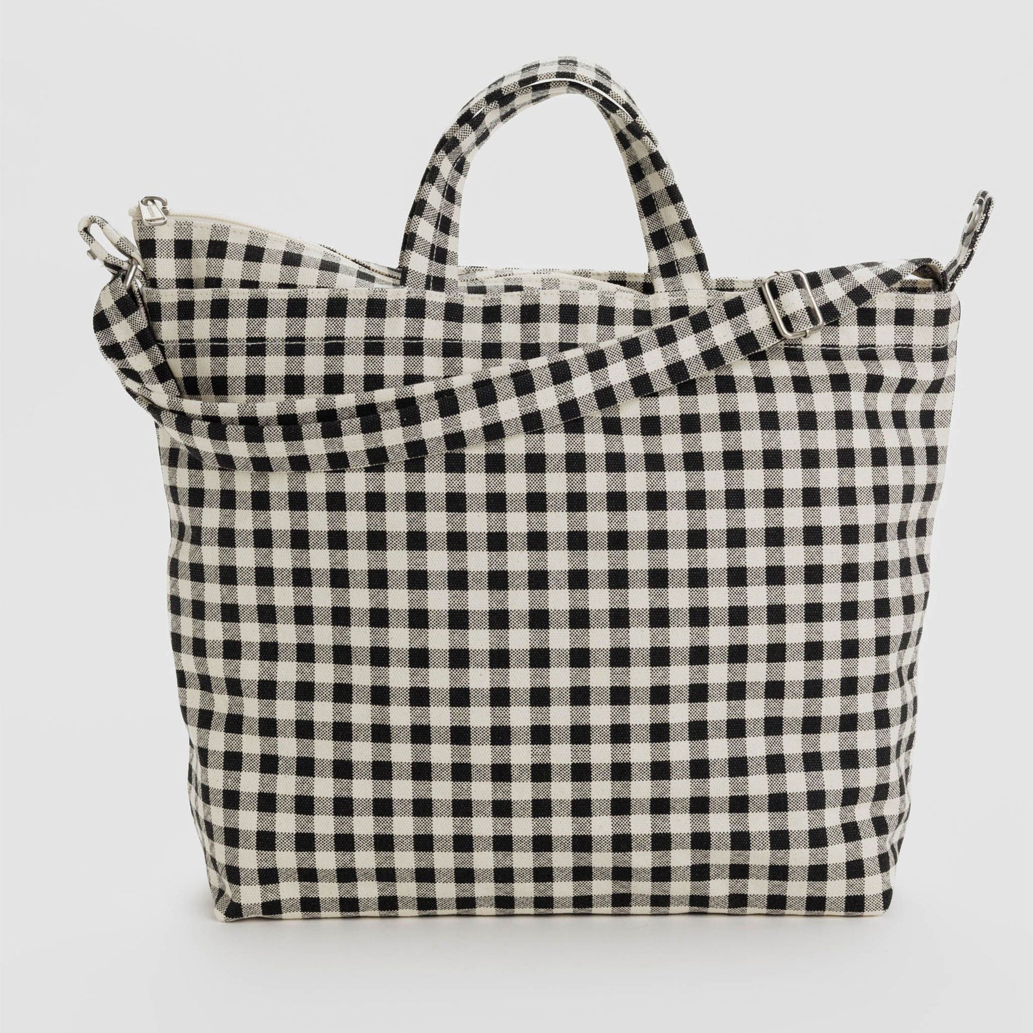 On a white background is a black and white gingham printed canvas bag with a hand strap and a longer adjustable shoulder strap. 