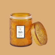 Flower textured gold translucent glass candle vessel with label, "Voluspa. Baltic Amber."