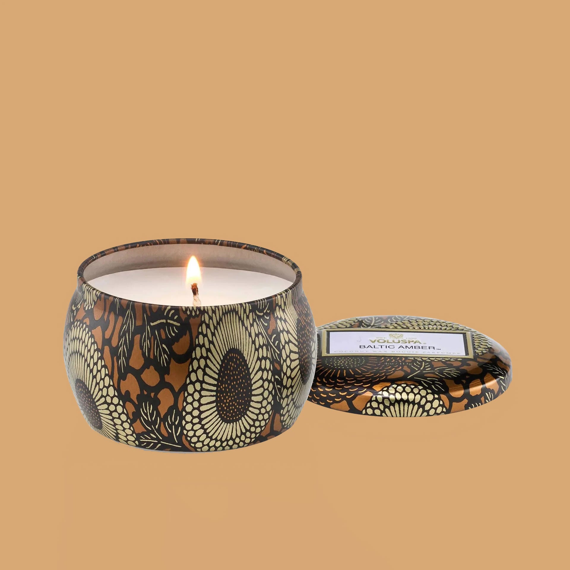Round tin candle vessel and lid with dark and light gold floral pattern and white wax candle.