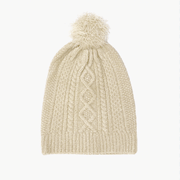 On a white background is an ivory knit beanie for dolls with a cable knit texture and a pom pom on top.