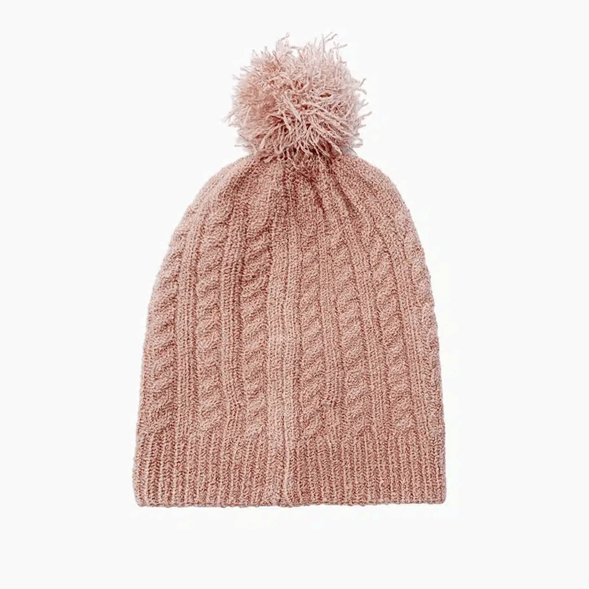 On a white background is a nude / pink knit beanie for dolls with a cable knit texture and a pom pom on top.