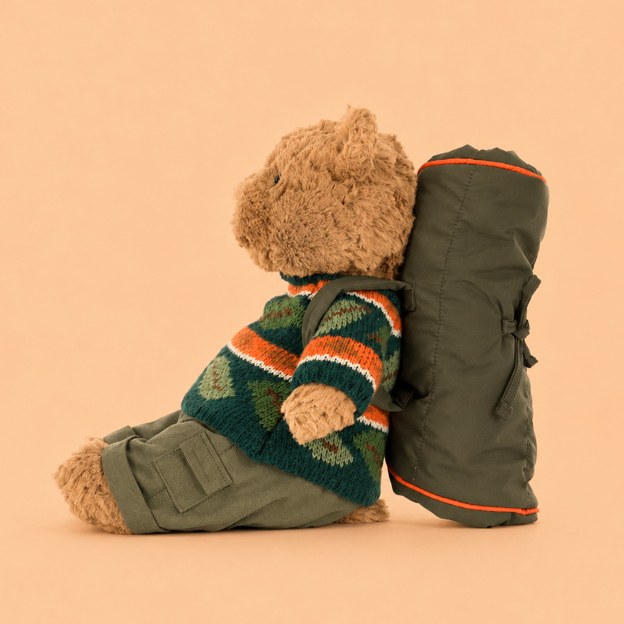 Teddy bear wearing a striped sweater and backpack on a beige background